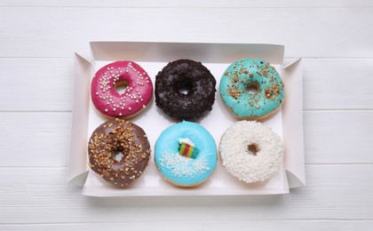 Box with different tasty glazed donuts on white wooden table, top view