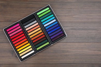 Photo of Set of colorful pastels in box on wooden table, top view with space for text. Drawing materials