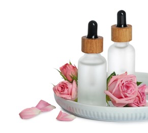 Photo of Bottles of essential rose oils and flowers on plate against white background