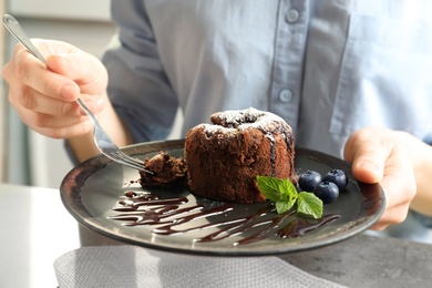 Woman eating delicious fresh fondant with hot chocolate at table. Lava cake recipe