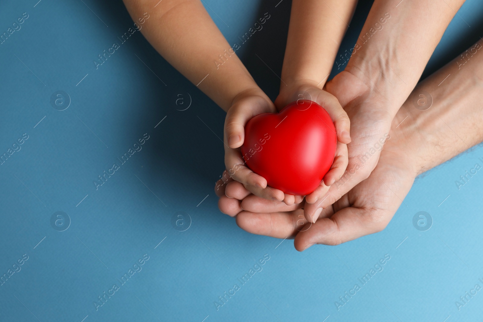 Photo of Father and his child holding red decorative heart on light blue background, top view. Space for text