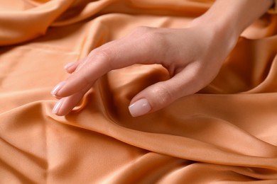 Photo of Woman touching soft orange fabric, closeup view