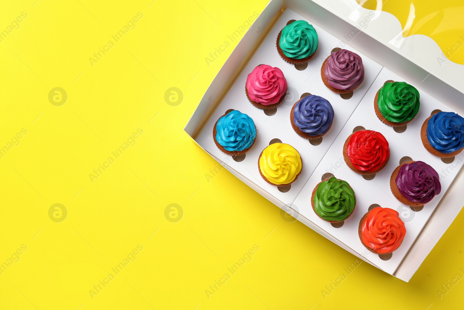 Photo of Box with different cupcakes on yellow background, top view. Space for text