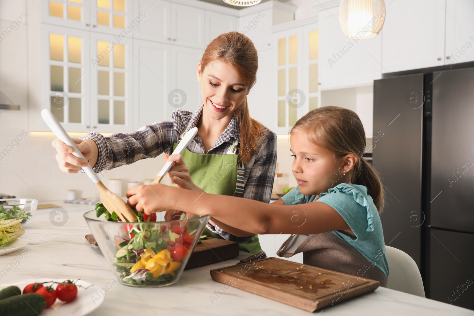 Photo of Mother and daughter cooking salad together in kitchen