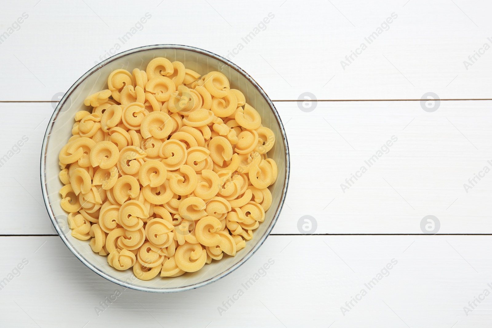 Photo of Raw dischi volanti pasta in bowl on white wooden table, top view. Space for text