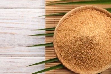 Photo of Coconut sugar, palm leaves and bamboo mat on wooden rustic table, top view. Space for text