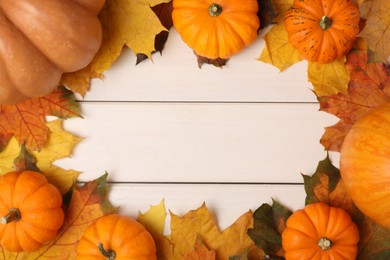 Frame of fresh ripe pumpkins and dry leaves on white wooden table, flat lay. Space for text