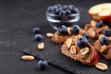 Photo of Fresh apples with peanut butter and blueberries on dark table, closeup. Space for text