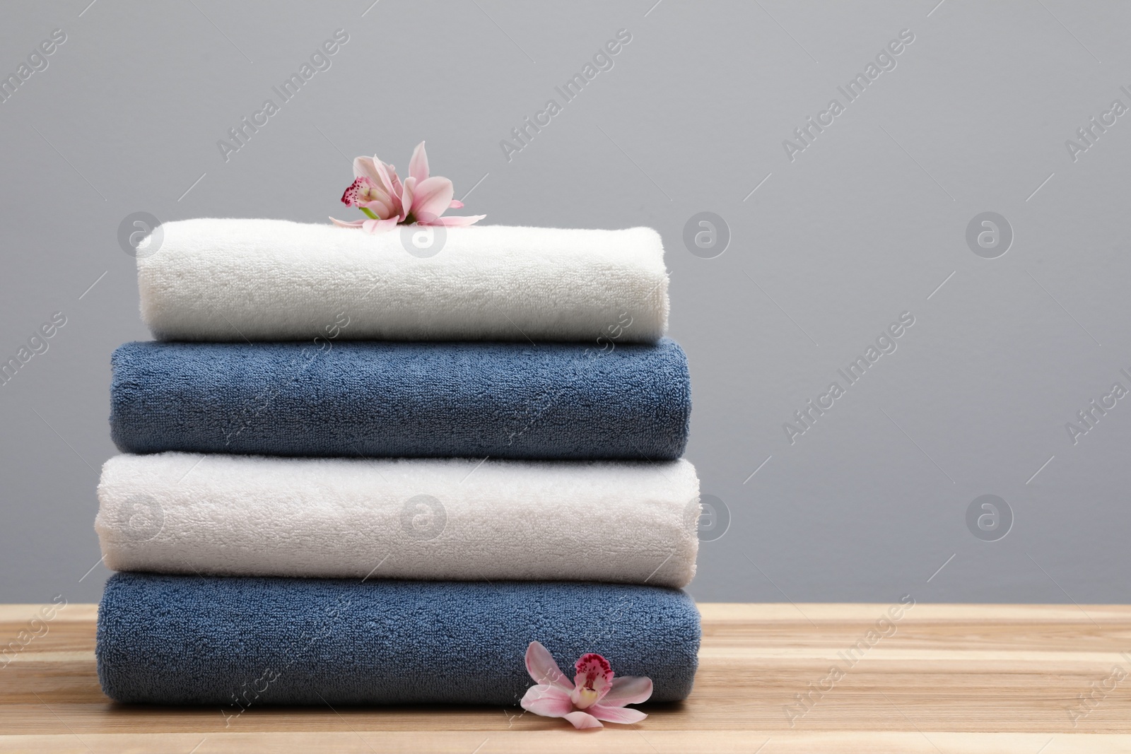 Photo of Stack of fresh towels with flowers on table. Space for text