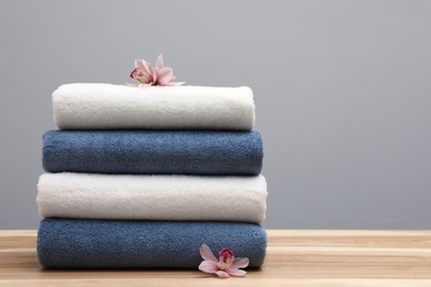 Stack of fresh towels with flowers on table. Space for text