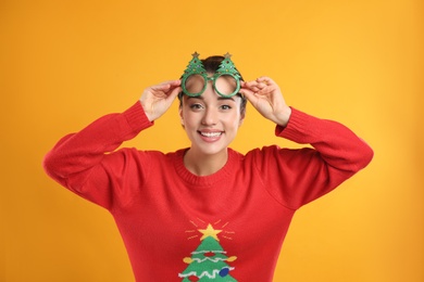Young woman in Christmas sweater and party glasses on yellow background