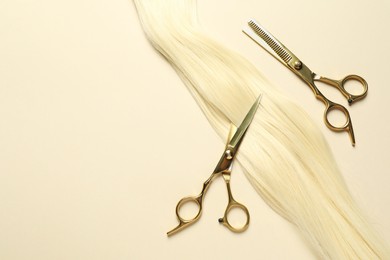 Photo of Professional scissors with blonde hair strand on beige background, flat lay. Space for text