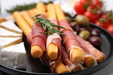 Photo of Delicious grissini sticks with prosciutto, cheese and olives on table, closeup