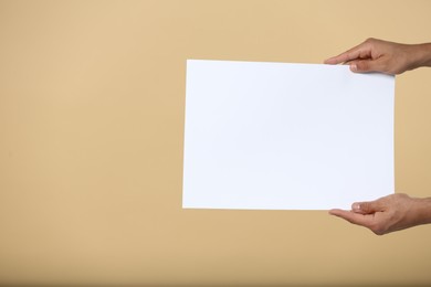 Photo of Man holding sheet of paper on beige background, closeup. Mockup for design