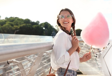 Photo of Young woman with cotton candy outdoors on sunny day. Space for text