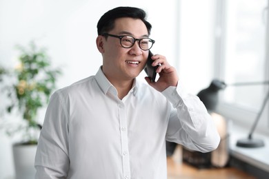 Portrait of smiling businessman talking by smartphone in office