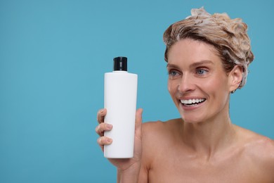 Photo of Washing hair. Portrait of beautiful happy woman with bottle on light blue background, space for text