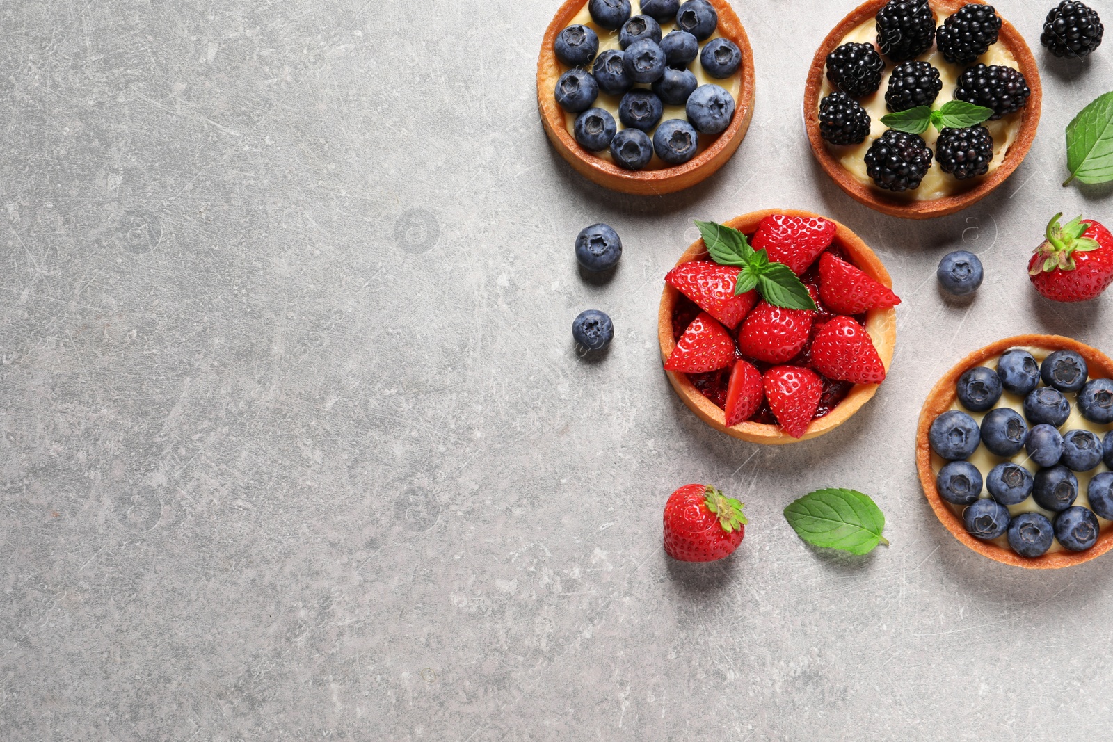 Photo of Tartlets with different fresh berries on light grey table, flat lay and space for text. Delicious dessert