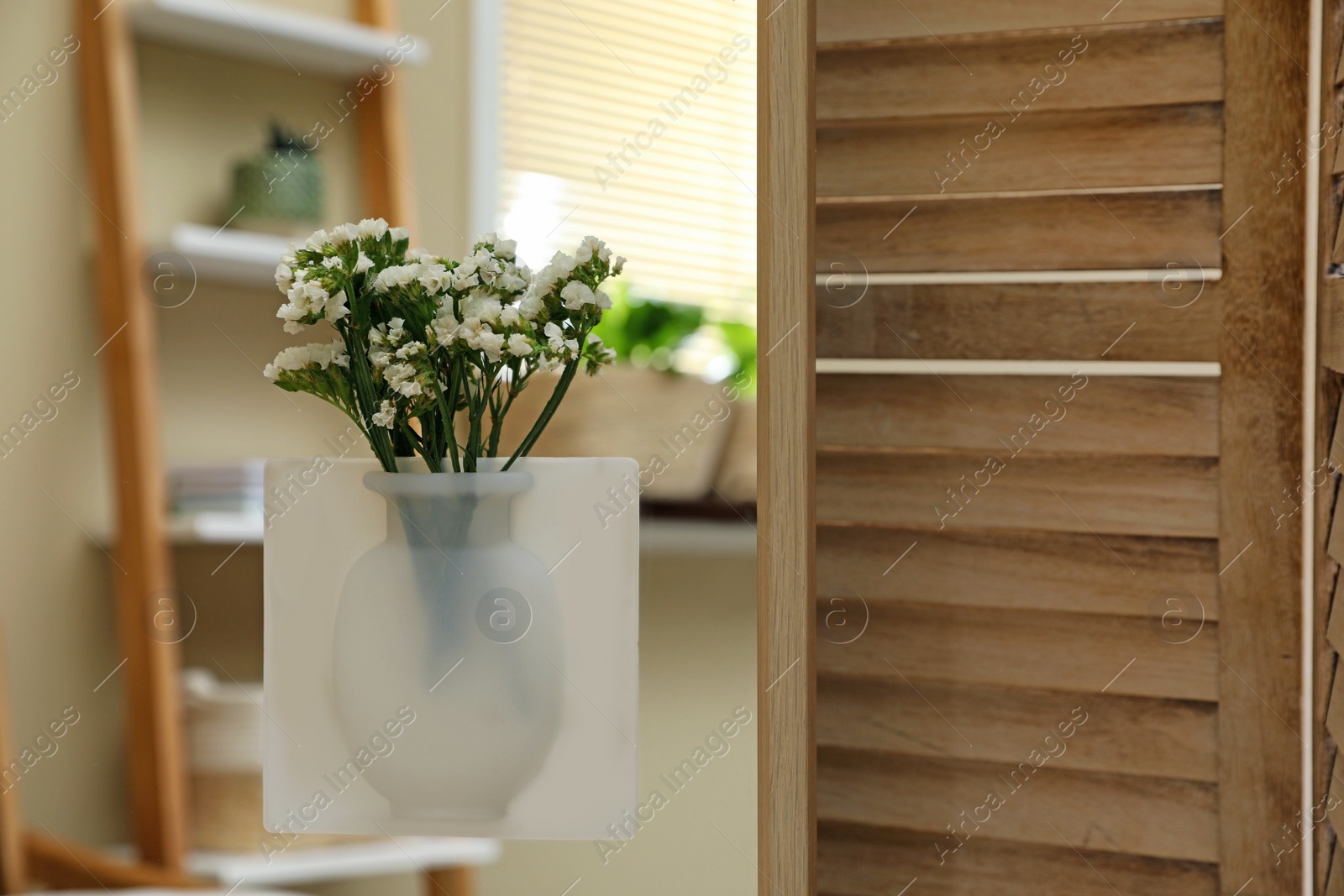 Photo of Silicone vase with beautiful white flowers on mirror in room