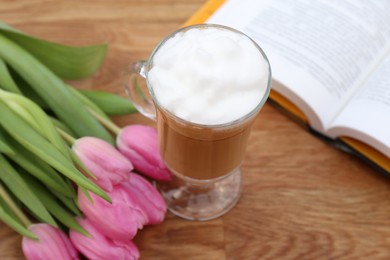 Photo of Glass of delicious cocoa, pink tulips and book on wooden table, closeup