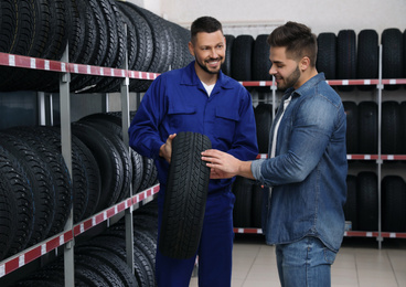 Mechanic helping client to choose car tire in auto store