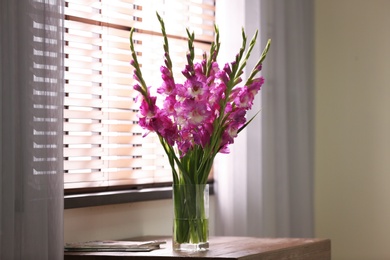 Photo of Vase with beautiful pink gladiolus flowers on wooden table in room, space for text