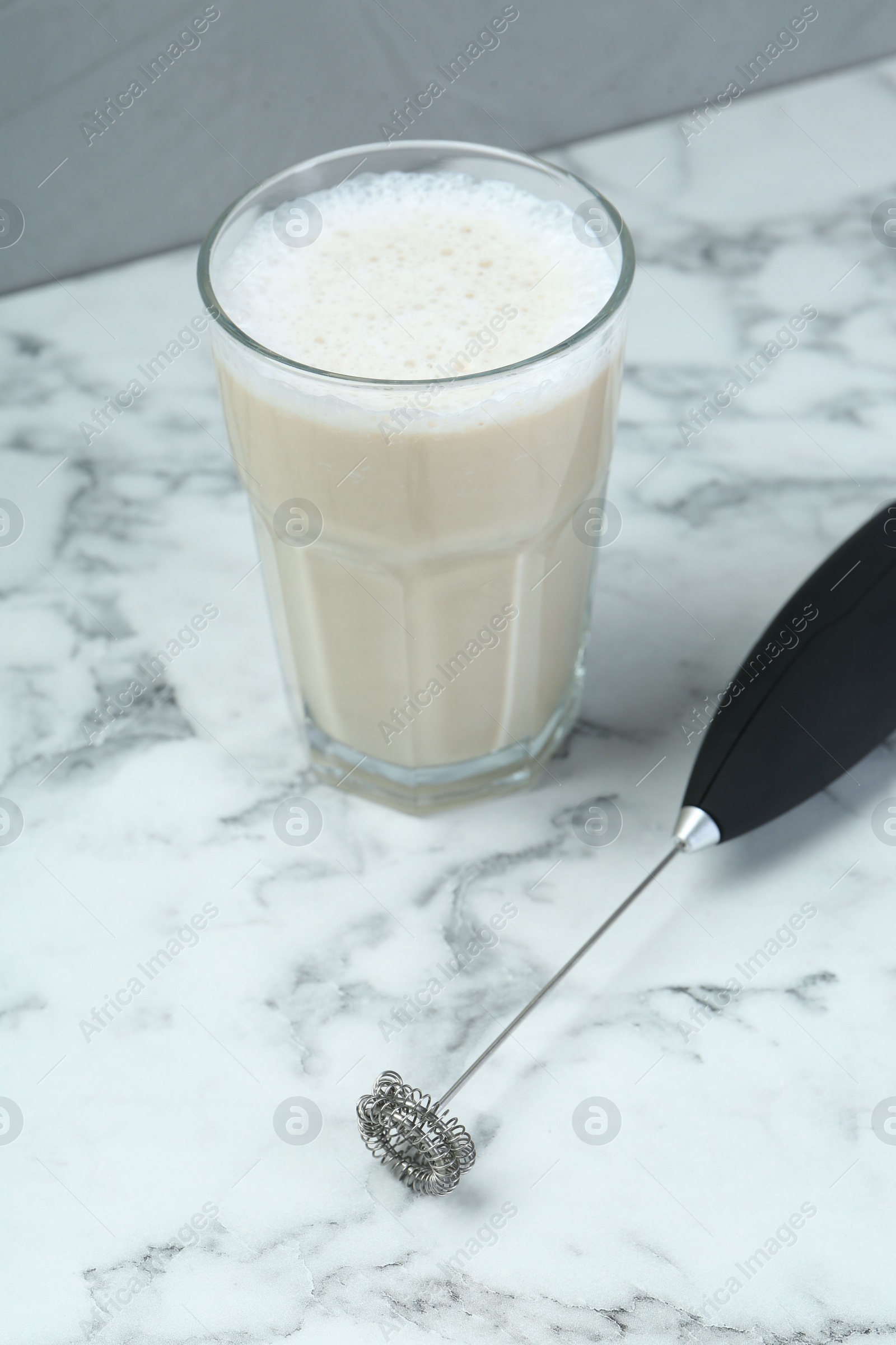 Photo of Mini mixer (milk frother) and tasty cappuccino in glass on white marble table