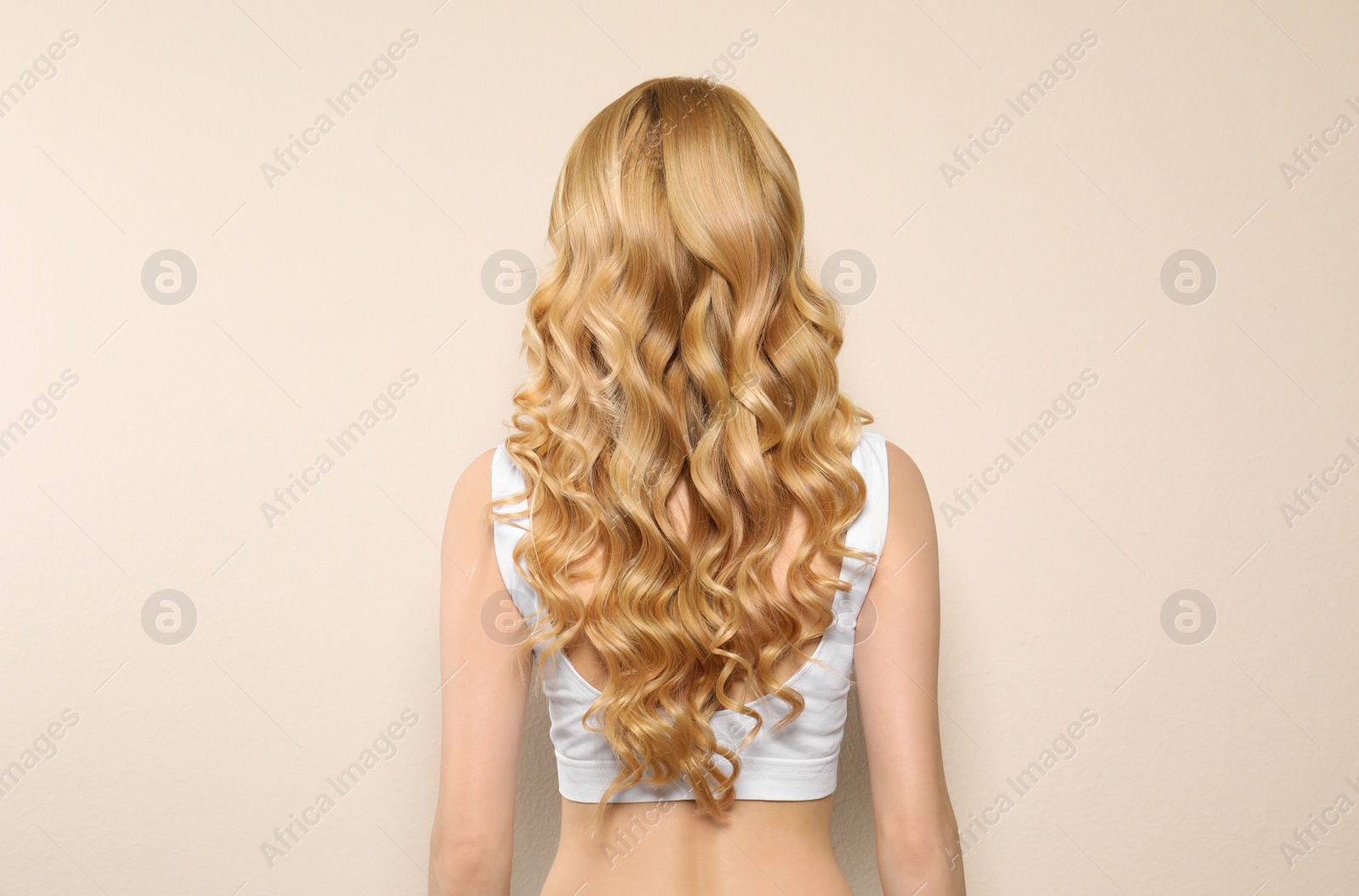 Photo of Young woman with long curly hair on beige background, back view