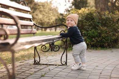 Little baby learning to walk near bench in park