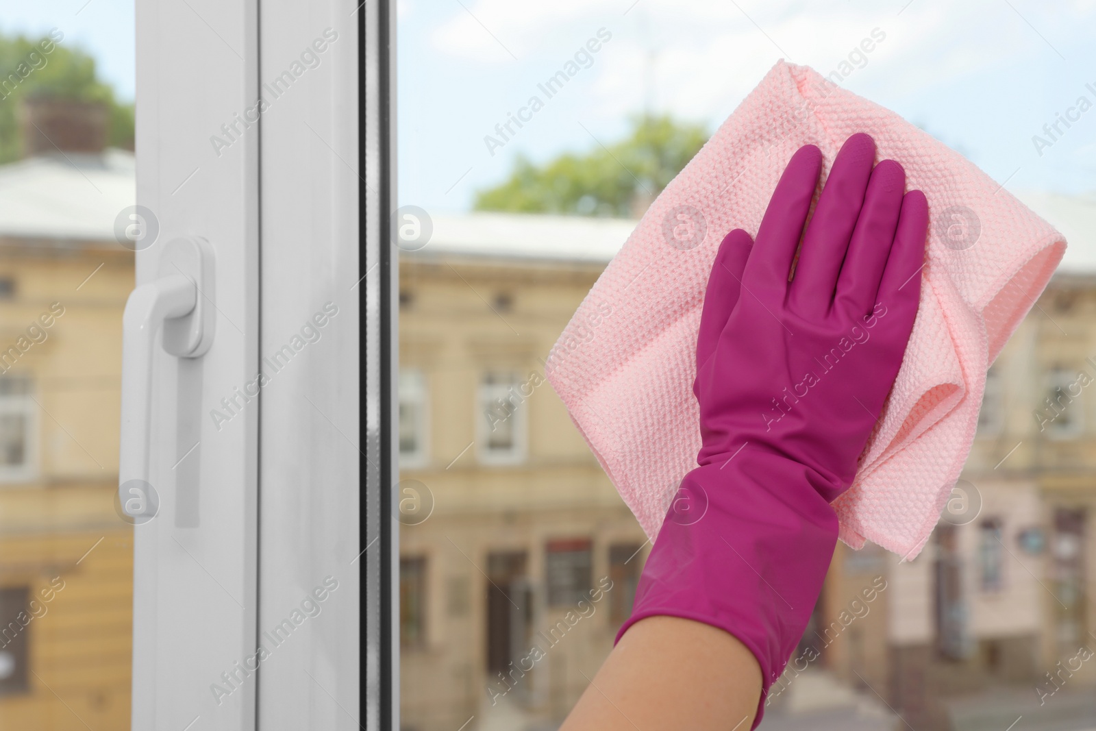 Photo of Young woman cleaning window glass with rag at home, closeup