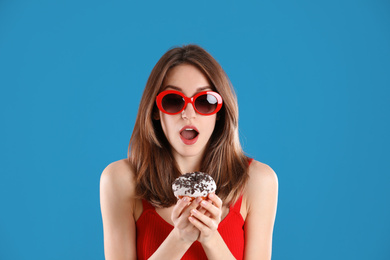 Beautiful young woman wearing sunglasses with donut on blue background