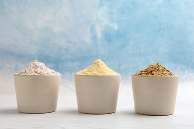 Bowls with different types of flour on table against color background. Space for text