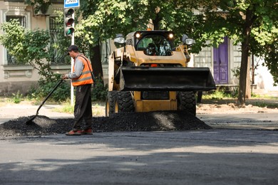 Photo of MYKOLAIV, UKRAINE - AUGUST 05, 2021: Worker laying new asphalt on city street. Road repair service
