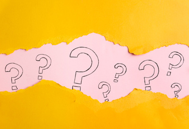 Photo of Question marks on pink background, view through hole in yellow paper