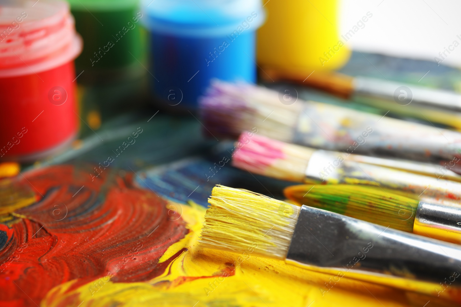 Photo of Different brushes and jars with paint on palette, closeup. Space for text