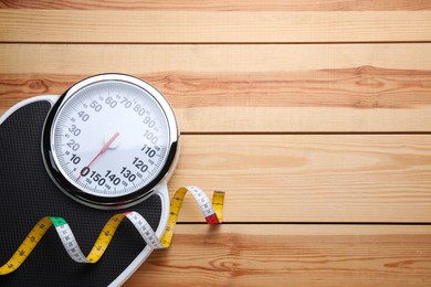 Bathroom scale, measuring tape and space for text on wooden floor, top view. Weight loss concept