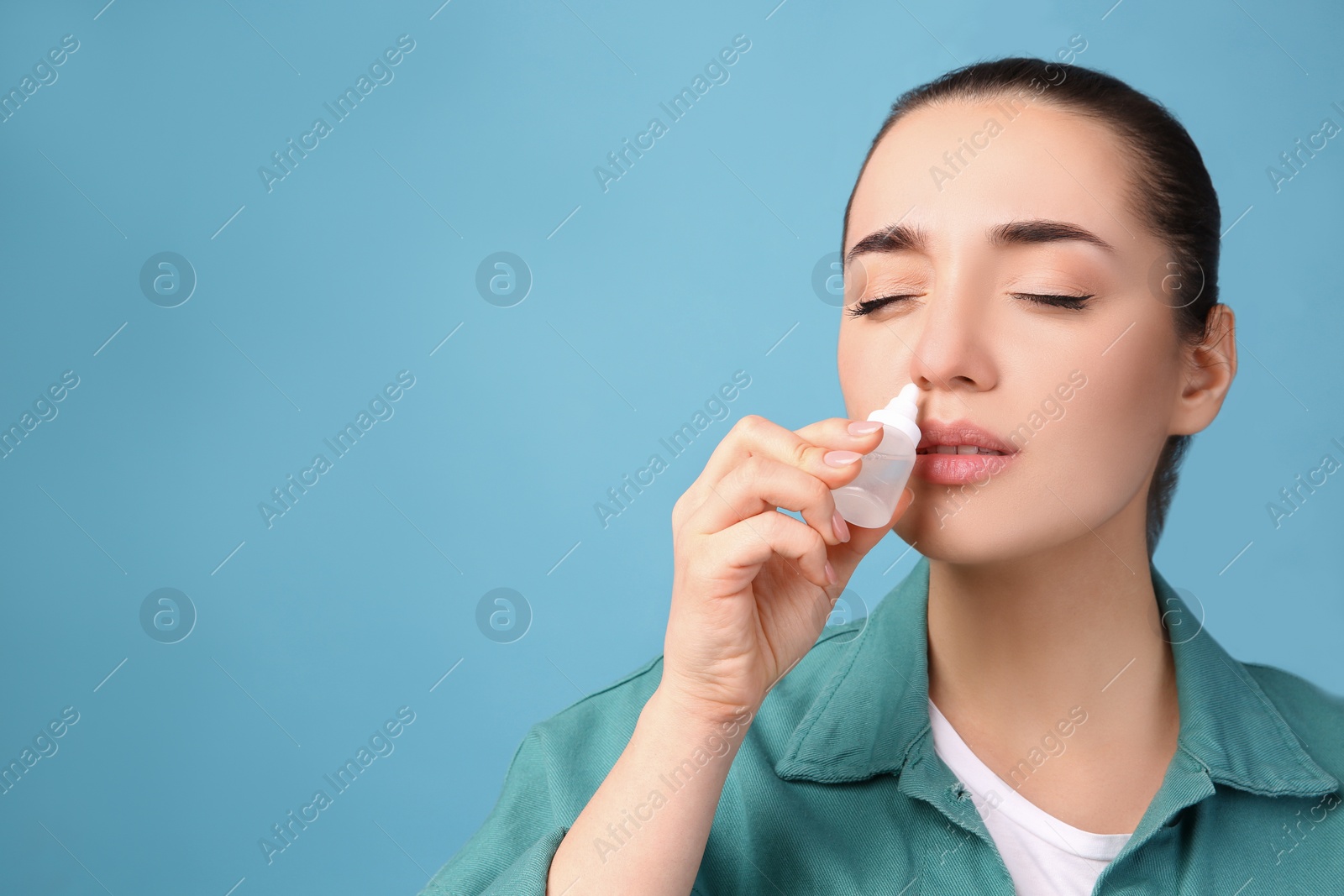 Photo of Woman using nasal spray on light blue background, space for text