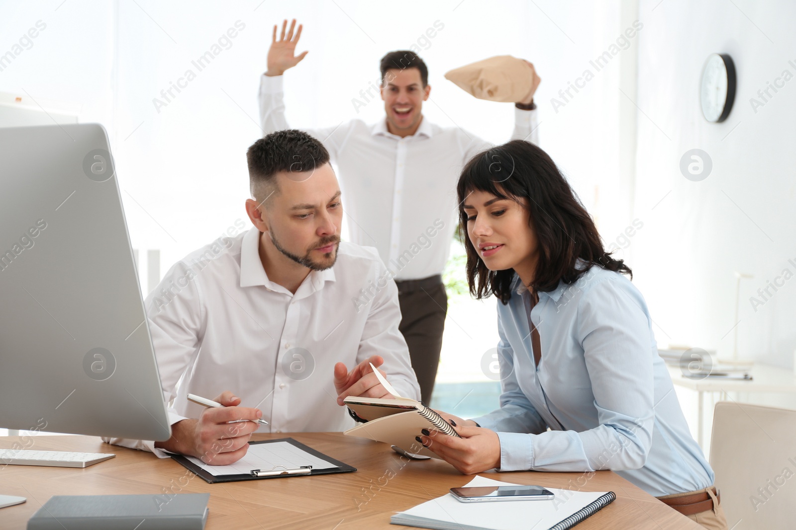 Photo of Man popping paper bag behind his colleagues in office. April fool's day