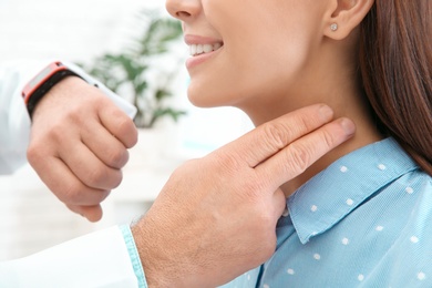 Doctor checking young woman's pulse with fingers in hospital, closeup