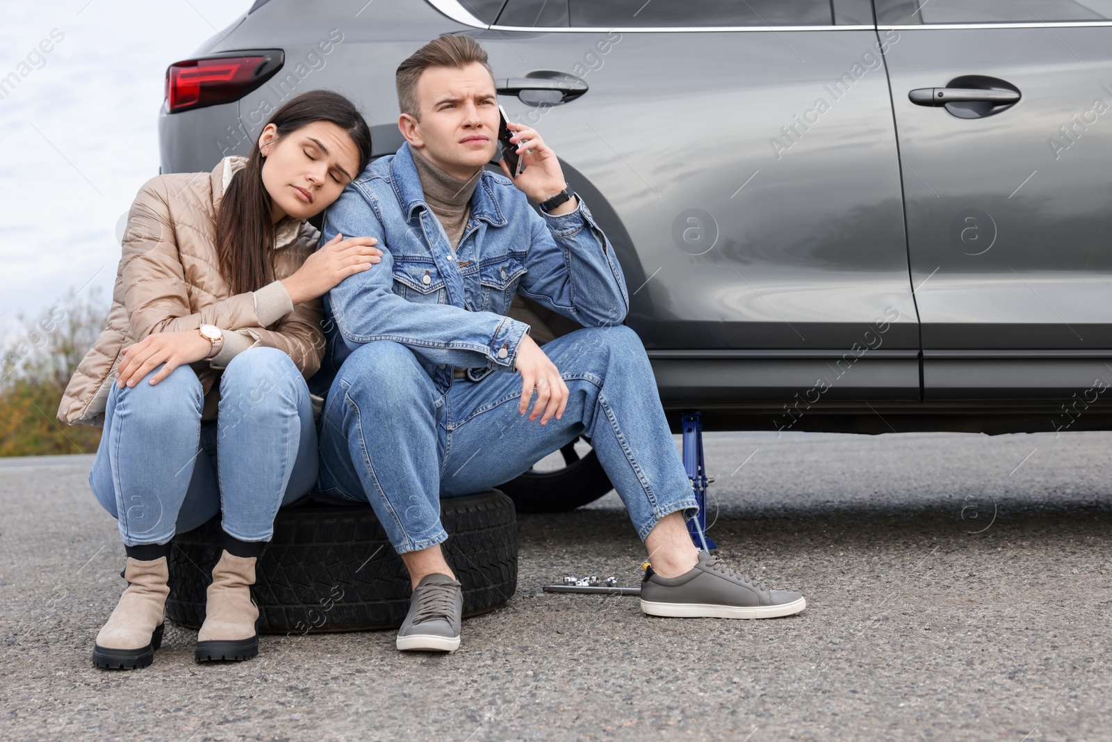 Photo of Young man calling to car service on roadside. Tire puncture