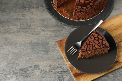 Photo of Piece of delicious chocolate truffle cake and fork on grey textured table, above view. Space for text