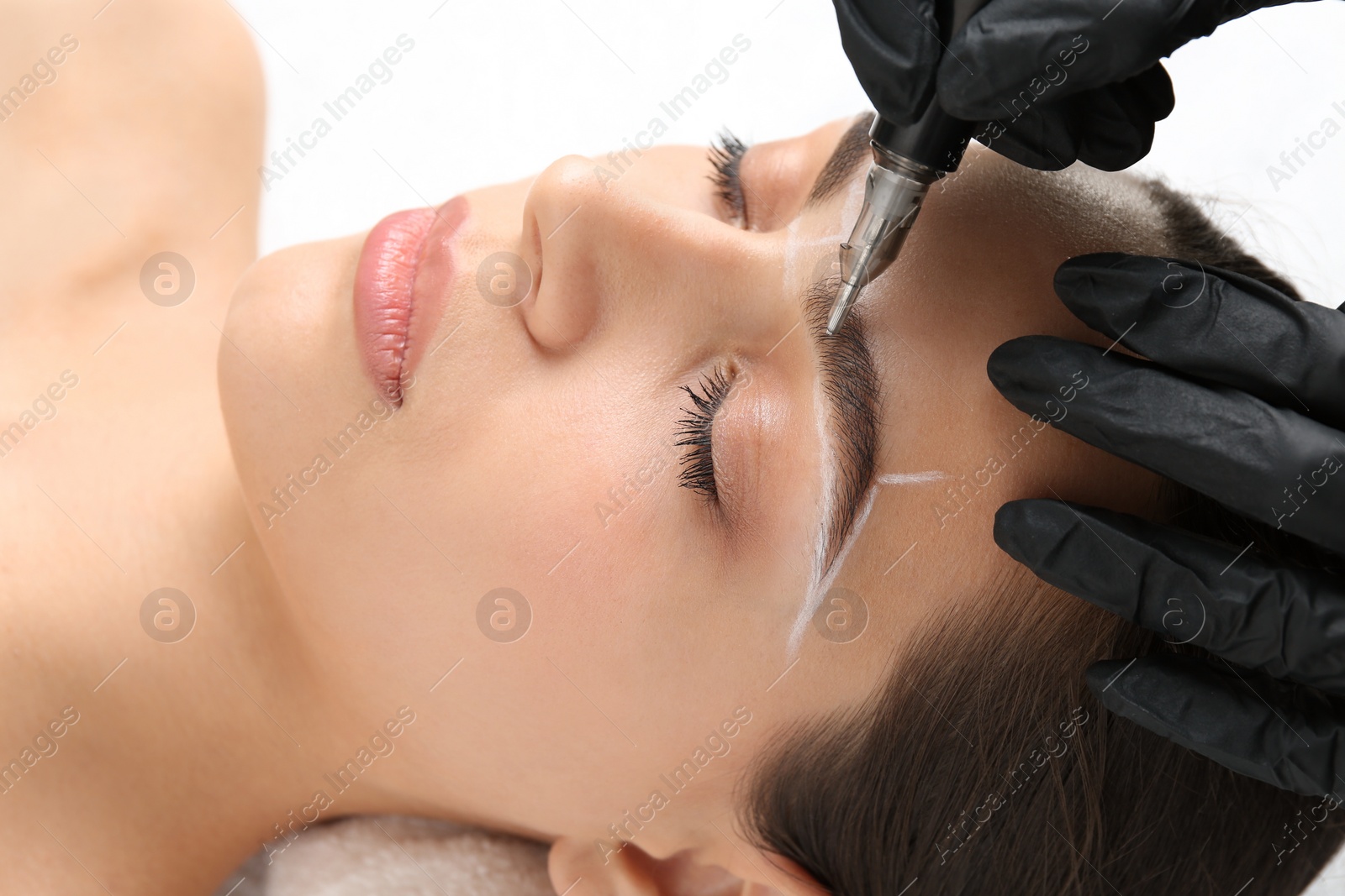 Photo of Beautician making permanent eyebrow makeup to young woman on white background, closeup