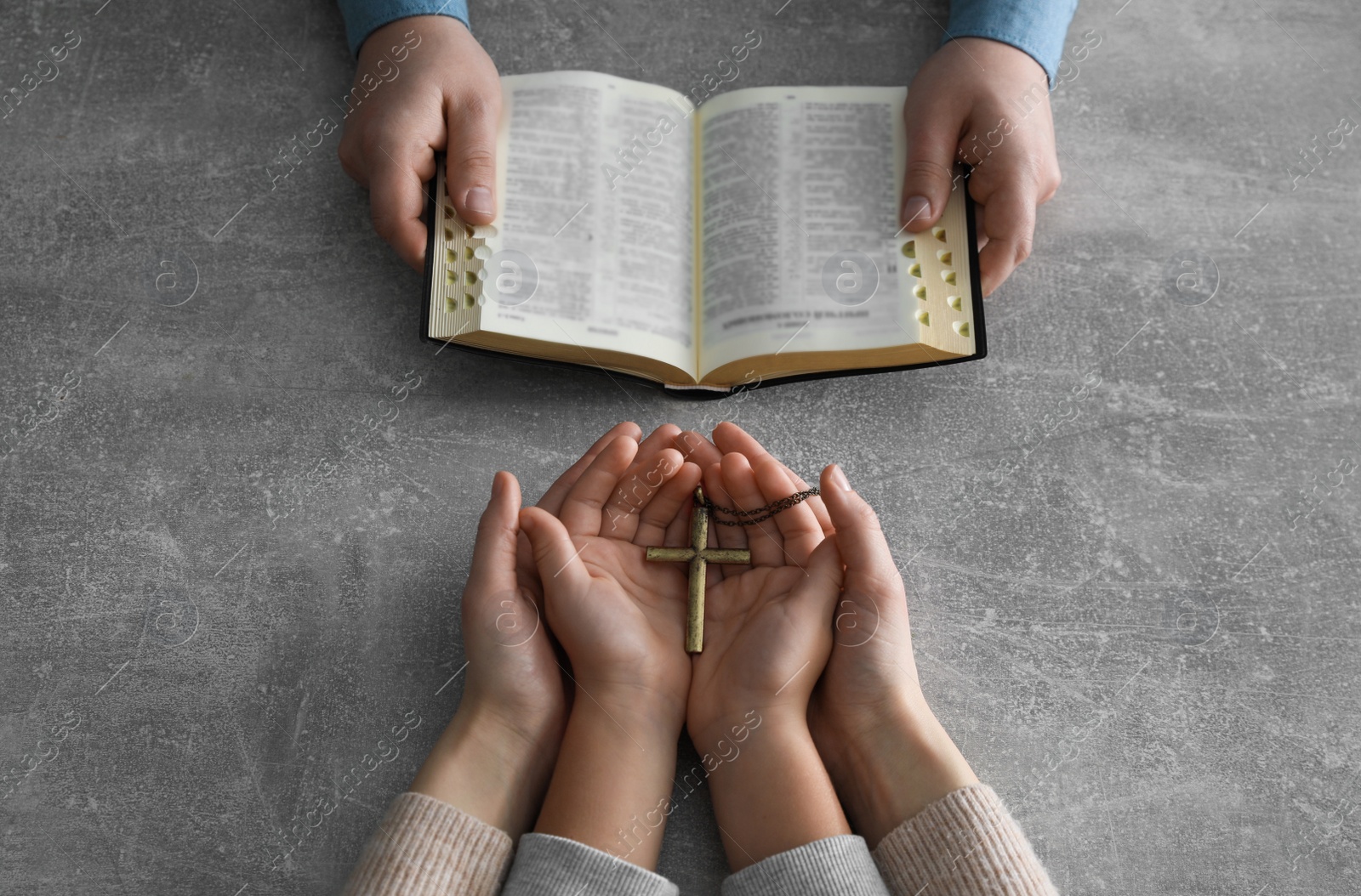 Photo of Boy praying and reading Bible with his godparents at grey table, closeup