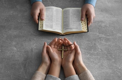 Photo of Boy praying and reading Bible with his godparents at grey table, closeup