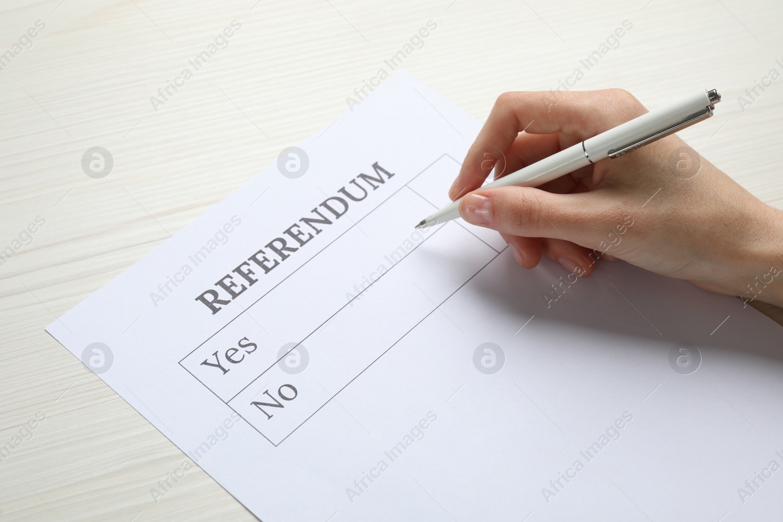 Photo of Woman with referendum ballot making decision at white wooden table, closeup