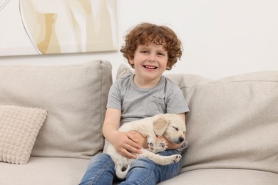 Little boy hugging cute puppy on couch indoors