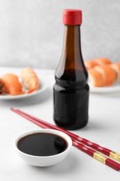 Tasty soy sauce, chopsticks and different types of sushi on white table