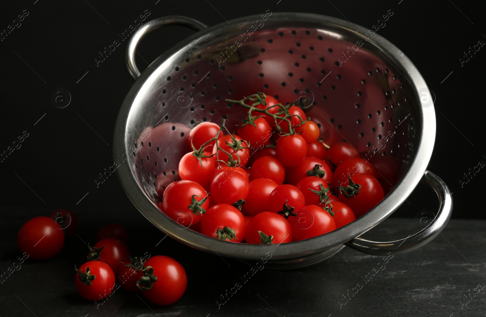 Photo of Fresh ripe cherry tomatoes and colander on black table