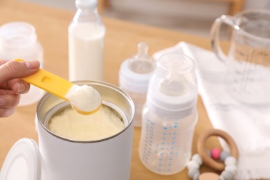 Woman preparing infant formula at table indoors, closeup. Baby milk