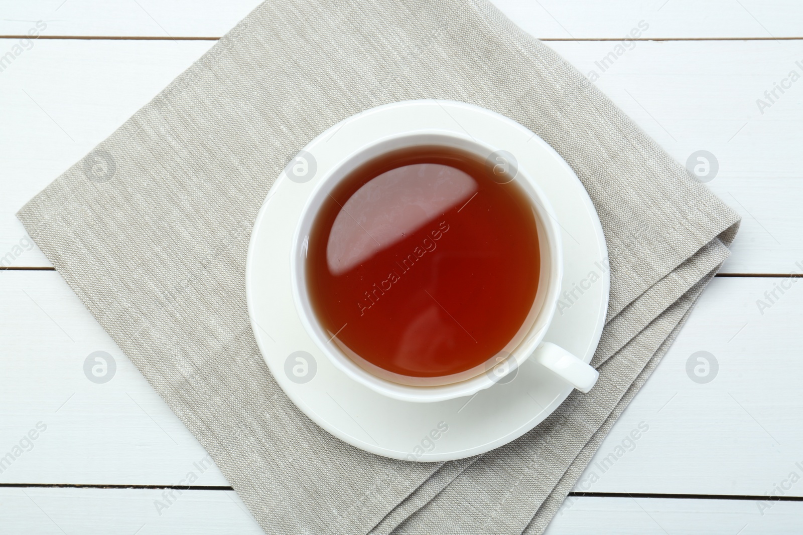 Photo of Aromatic tea in cup on white wooden table, top view